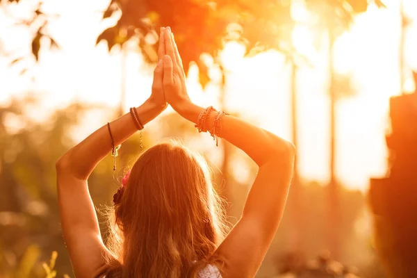 Woman holding hands in the air with orange sunlight in the background.