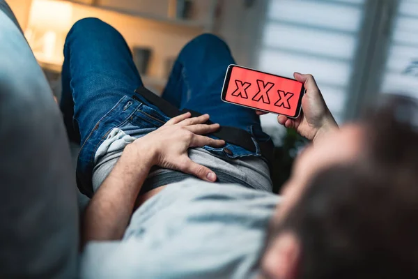 Man holding modern smartphone / cellphone and watching XX videos on a home couch. Taboo still in modern times.