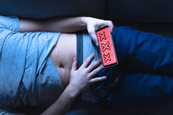 Man holding modern smartphone / cellphone and watching XX videos on a home couch. Taboo still in modern times.