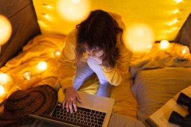 Oturma odasındaki ev yapımı çadırının altında dizüstü bilgisayar kullanan 11 yaşında bir kız..