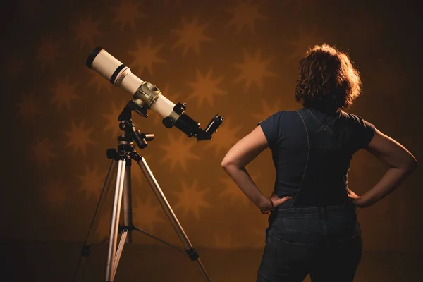 Woman looking at the stars through a telescope- astrology concept, horoscope predictions about the future.