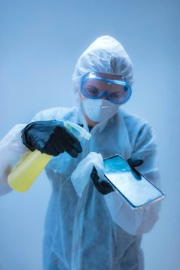 Tıp doktoru, akıllı telefon dezenfeksiyonu için antiseptik doku taşıyan virüs ve hastalıklardan korunmak için tam vücut kıyafeti giyen bilim adamı..
