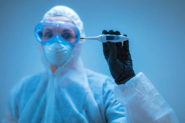 Tıbbi doktor, vücut ısısını ölçmek için termometre tutan virüslerden ve hastalıklardan korunmak için giysi giyen bilim adamı..