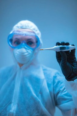 Tıbbi doktor, vücut ısısını ölçmek için termometre tutan virüslerden ve hastalıklardan korunmak için giysi giyen bilim adamı..