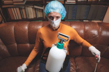 Koruyucu antiviral maskeli kadın, kimyasal dezenfekte spreyi şişesi ev izolasyonunda..