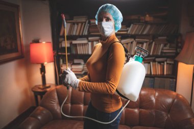 Koruyucu antiviral maskeli kadın, kimyasal dezenfekte spreyi şişesi ev izolasyonunda..