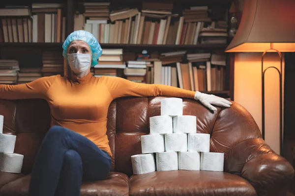 Woman with protective antiviral mask and a reserve of toilet paper waiting anxious in home isolation.