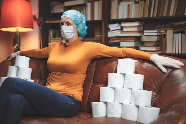 Woman with protective antiviral mask and a reserve of toilet paper waiting anxious in home isolation.