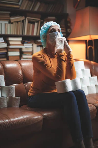 Woman with protective antiviral mask and a reserve of toilet paper waiting anxious in home isolation.