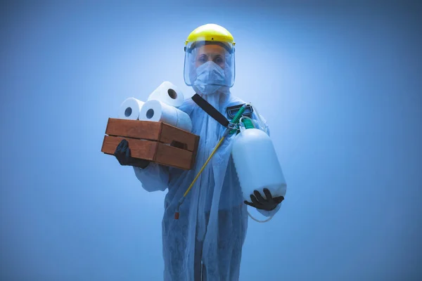 保護スーツとフェイスマスクを持つ人科学者 ウイルス 細菌に対する除染のためのバイオハザードスプレー 家庭でのトイレットペーパーのストックのパラノイア 日の終わりを待っている — ストック写真