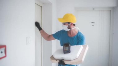 Koruyucu tıbbi maskeli teslimatçı elinde pizza kutusu ve POS kablosuz terminali ile kart ödeme, kapı çalma - virüsler ve salgın, evinize yiyecek teslimatı ve güvenlik önlemleri.