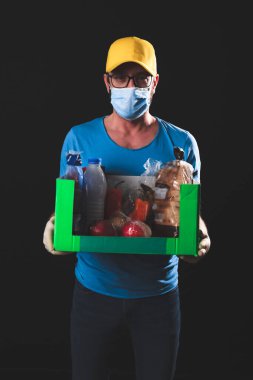 Salgın ve tecrit karantinası sırasında koruyucu maskeli bir teslimatçı elinde yiyecek kutusuyla....