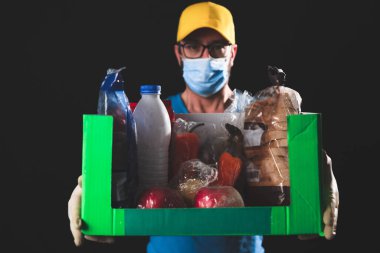 Salgın ve tecrit karantinası sırasında koruyucu maskeli bir teslimatçı elinde yiyecek kutusuyla....