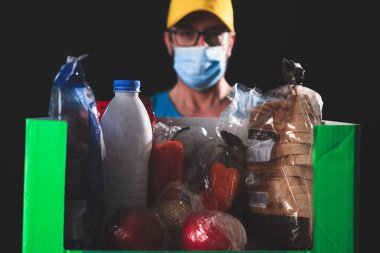 Salgın ve tecrit karantinası sırasında koruyucu maskeli bir teslimatçı elinde yiyecek kutusuyla....