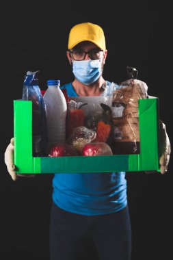 Salgın ve tecrit karantinası sırasında koruyucu maskeli bir teslimatçı elinde yiyecek kutusuyla....