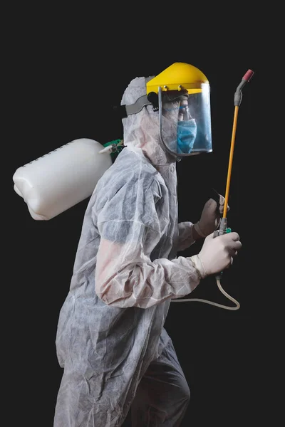 Person with protective antiviral mask, suit, helmet and chemical decontamination sprayer bottle in home isolation.