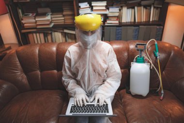 Koruyucu antiviral maskeli ve üniformalı bir kadın evde dizüstü bilgisayar kullanıyor, çalışıyor, gazete okuyor, internette sörf yapıyor, internetten yemek sipariş ediyor..