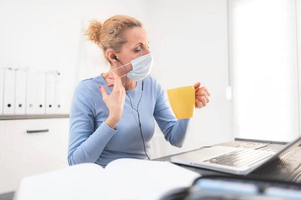 Online teacher with a protective mask tutoring over the internet. Trouble with drinking morning coffee.