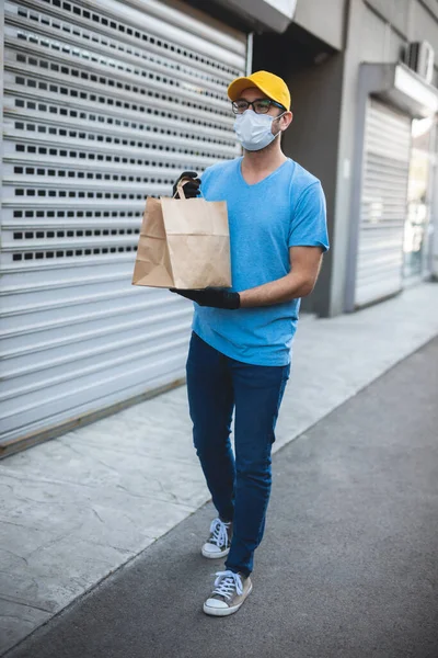 送货员带着防护面罩和手套 拿着装有食品杂货的盒子 袋子在大楼前面 — 图库照片
