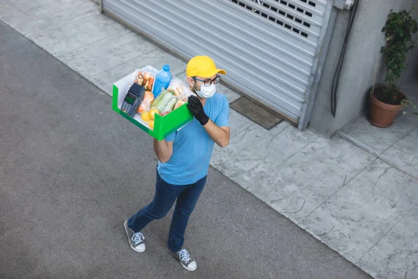 Delivery guy with protective mask holding box / bag with groceries and POS for contactless payment.