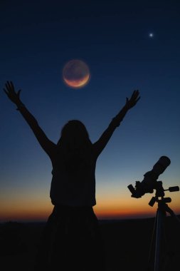 Bir kadın silueti ve alacakaranlık gökyüzü ile teleskop.