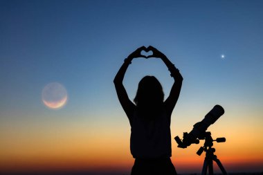 Bir kadın silueti ve alacakaranlık gökyüzü ile teleskop.