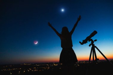 Bir kadın silueti ve alacakaranlık gökyüzü ile teleskop.