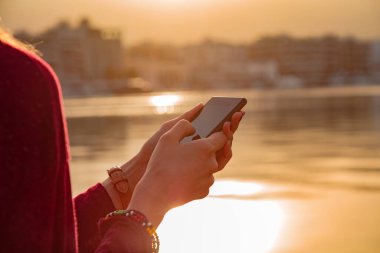 Şehirdeki su koyunun yanında cep telefonu kullanan genç bir kadın..