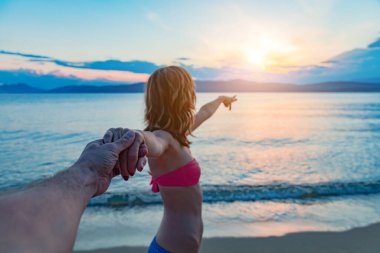 Kız arkadaş ve erkek arkadaş kumsalda el ele tutuşuyorlar..