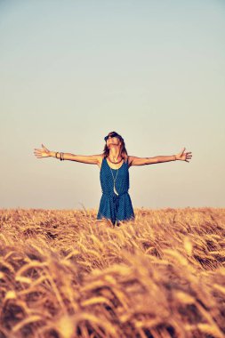 Genç bir kadın buğday tarlasında zıplıyor ve eğleniyor.
