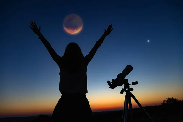 Silhouette of a woman and telescope with twilight sky.