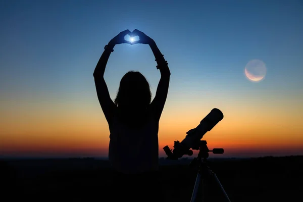 Silhouette of a woman and telescope with twilight sky.