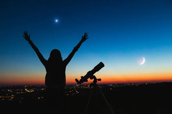 Silhouette of a woman and telescope with twilight sky.