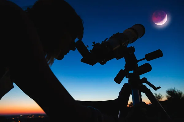 Silhouette of a woman and telescope with twilight sky.