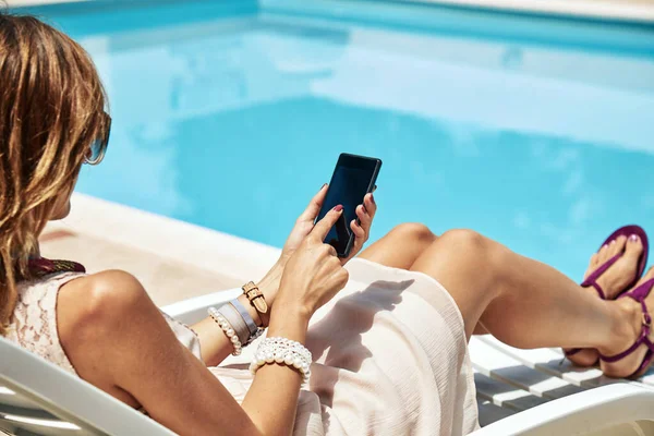 stock image Young woman using cellphone near the swimming pool.