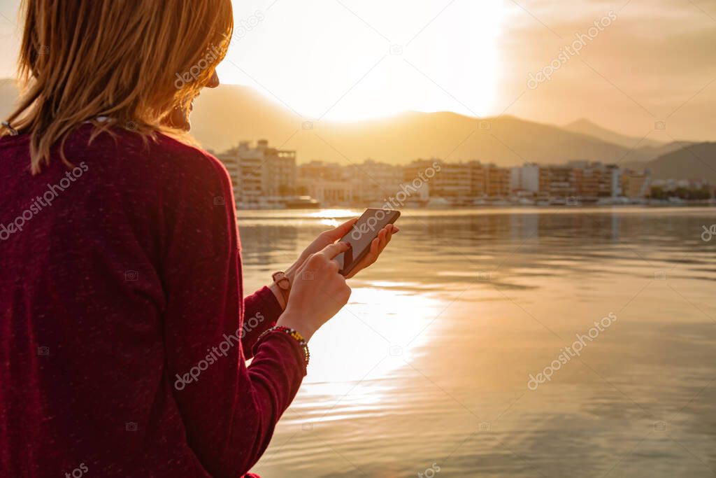 Young woman using cellphone near water bay in urban area.