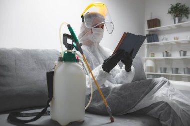Koruyucu antiviral maske, kostüm, kask ve kimyasal dezenfekte spreyini evde izolasyon şişesinde giyen kişi okuyor..