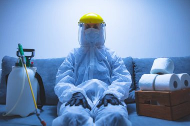 Klozet kağıdı stoğu ve koruyucu antiviral maskesi olan kişi, kask, kimyasal dezenfekte spreyi ve ev izolasyonu şişesi..