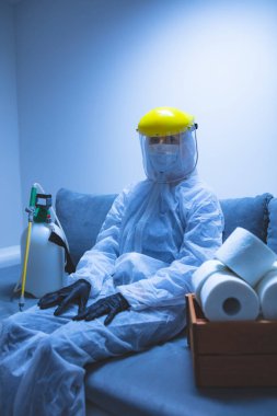 Klozet kağıdı stoğu ve koruyucu antiviral maskesi olan kişi, kask, kimyasal dezenfekte spreyi ve ev izolasyonu şişesi..