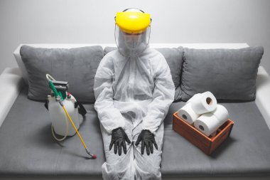 Klozet kağıdı stoğu ve koruyucu antiviral maskesi olan kişi, kask, kimyasal dezenfekte spreyi ve ev izolasyonu şişesi..