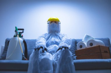 Klozet kağıdı stoğu ve koruyucu antiviral maskesi olan kişi, kask, kimyasal dezenfekte spreyi ve ev izolasyonu şişesi..