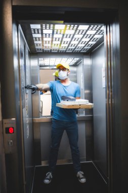 Koruyucu tıbbi maskeli teslimatçı elinde pizza kutusu tutuyordu. Virüsler ve salgınlarla dolu günler, evinize yiyecek teslimatı..