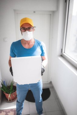 Koruyucu tıbbi maskeli teslimatçı elinde pizza kutusu tutuyordu. Virüsler ve salgınlarla dolu günler, evinize yiyecek teslimatı..