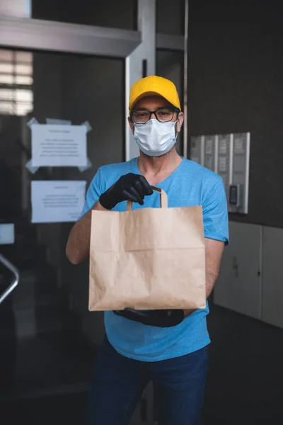 送货员带着防护面罩和手套 拿着装有食品杂货的盒子 袋子在大楼前面 — 图库照片