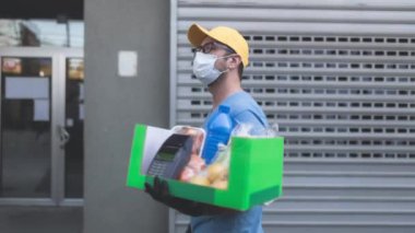 Koruyucu maskeli teslimatçı. Bakkaliye ve POS 'la dolu bir çanta tutuyor..