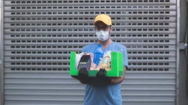 Koruyucu maskeli teslimatçı. Bakkaliye ve POS 'la dolu bir çanta tutuyor..