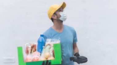 Koruyucu maskeli teslimatçı. Bakkaliye ve POS 'la dolu bir çanta tutuyor..