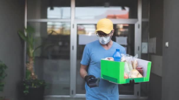 送货员带着防护面罩 拿着装有杂货和非接触式付款的盒子 — 图库视频影像