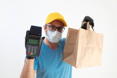 Koruyucu maskeli teslimatçı. Bakkaliye ve POS 'la dolu bir çanta tutuyor..