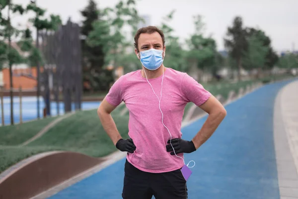 의료용 마스크와 장갑을 스마트폰과 이어폰을 사용하고 환경에서 조깅을 — 스톡 사진